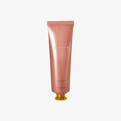 Pink hand cream tube with gold cap on a light gray background