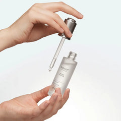 Hand holding a Novage skincare dropper bottle with a white background