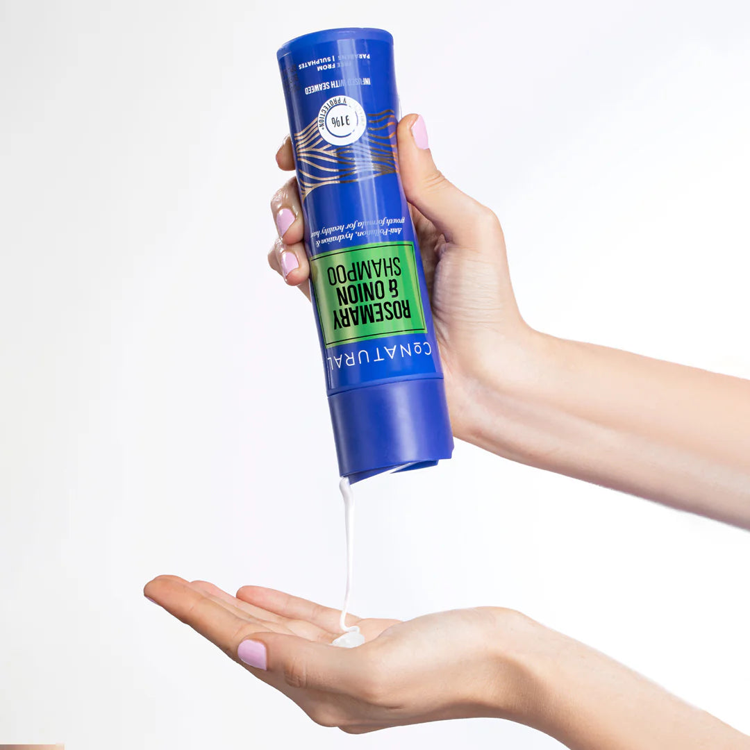 Hand holding a blue and green shampoo can with white liquid being dispensed onto another hand against a white background
