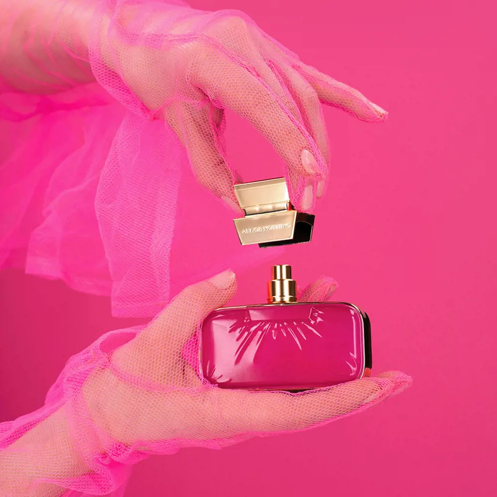 Pink perfume bottle with gold cap held by a hand against a pink background