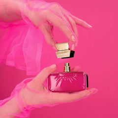 Pink perfume bottle with gold cap held by a hand against a pink background