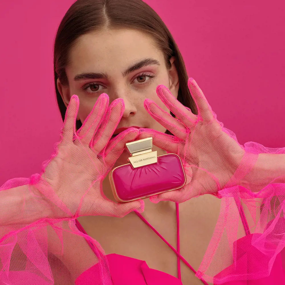 Woman holding a pink and gold perfume bottle against a pink background
