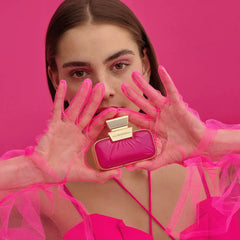 Woman holding a pink and gold perfume bottle against a pink background