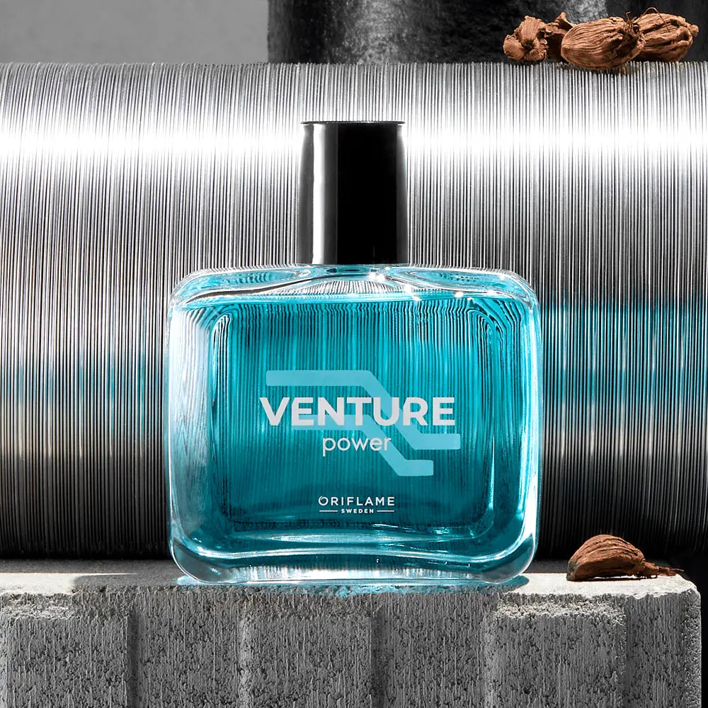 Blue 'Venture Power' perfume bottle by Oriflame on a textured surface with a metallic background.