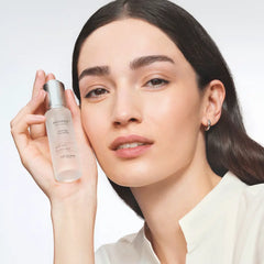 Woman holding a skincare bottle with a plain background