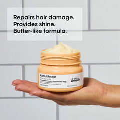 L'Oreal Absolut Repair mask jar held in a hand with text about hair care benefits on a tiled wall background