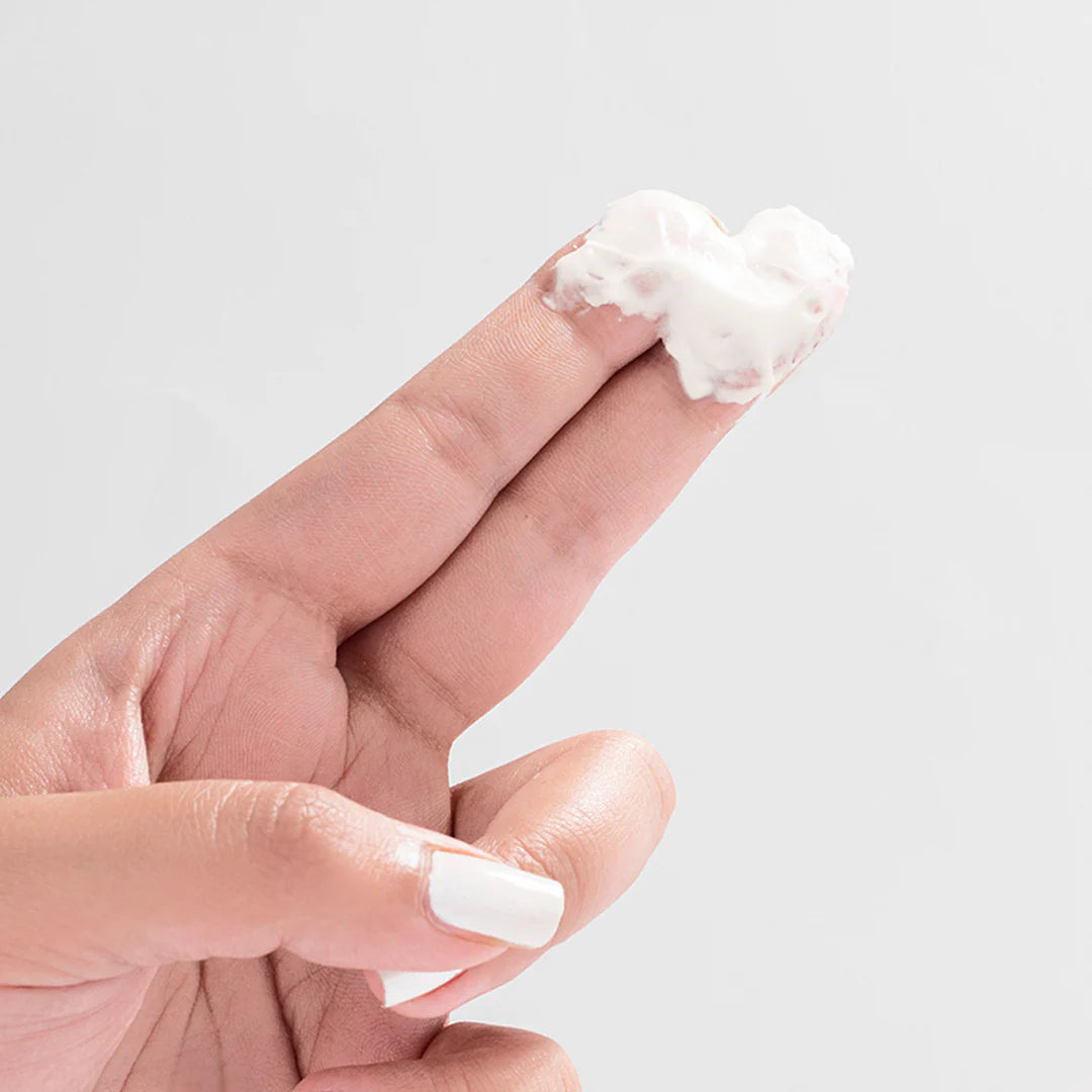 Hand holding a small amount of white cream on a light gray background