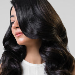 Woman with long, wavy black hair covering her face on a gray background