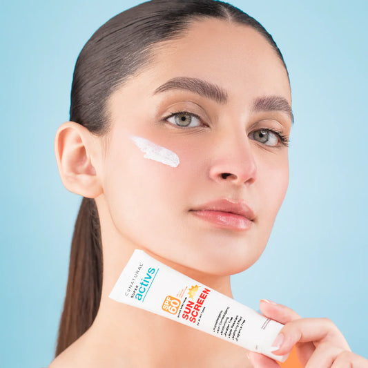 Woman applying sunscreen to her face with a tube of sunscreen in front of a blue background