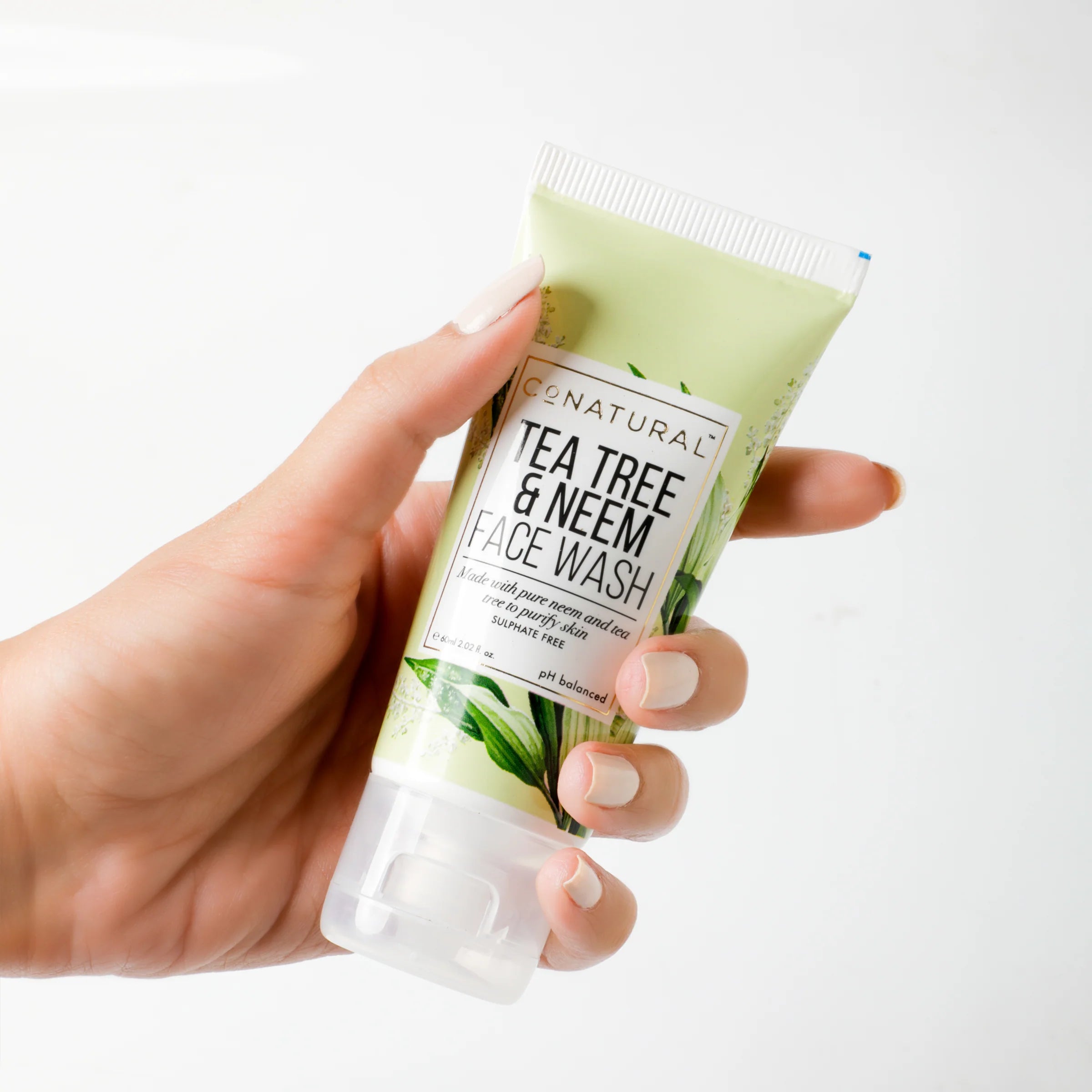 Hand holding a tube of Cenatural Tea Tree & Neem Face Wash against a white background